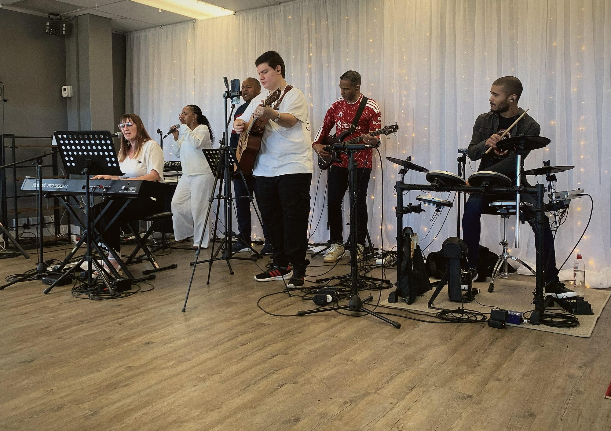 The worship band leading on keys, vocals, guitars and drums in front of a curtain of fairy lights.